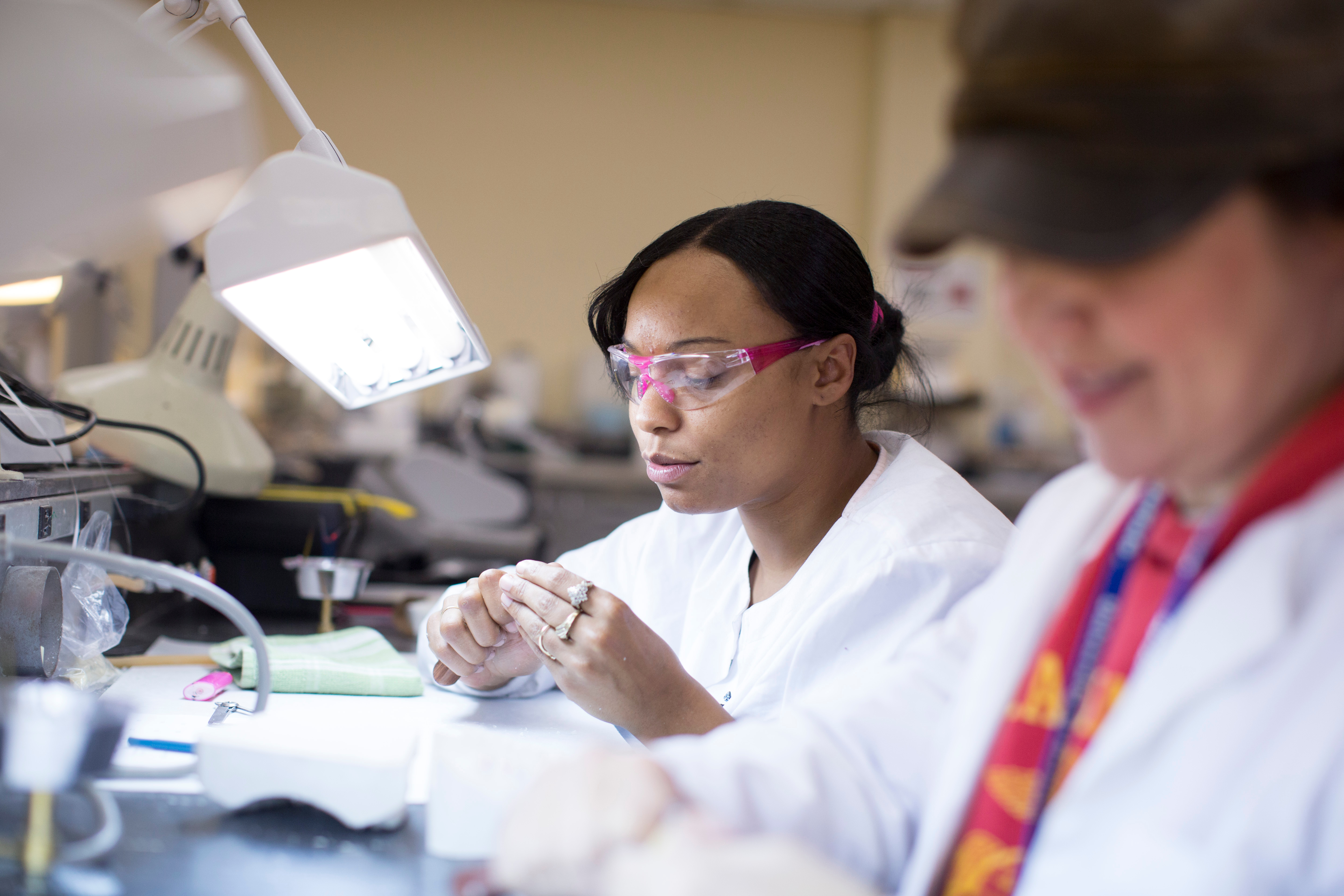 A dental hygiene student wearing protective eyewear works on a hands-on lab exercise at a workstation, while another student collaborates nearby in a clinical classroom setting at SUNY Erie.