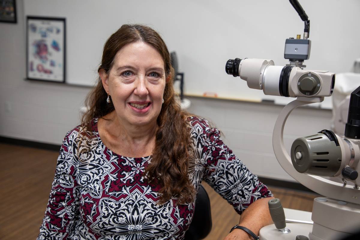 Professor Janet Acara sitting next to an optometry device.
